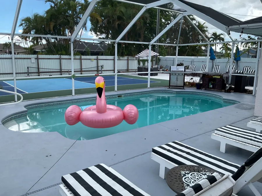 Screened pool with a pink flamingo float and striped loungers, court behind